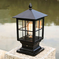 Vintage black outdoor post lantern with glass panels and Edison bulb mounted in a garden
